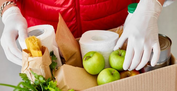 Volunteer in the protective medical mask and gloves putting food In donation box.